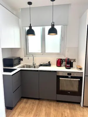 a kitchen with white cabinets and a sink and two lights at Zeus Downtown Hub with Panoramic View in Nicosia