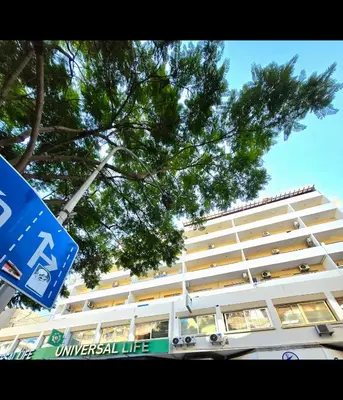 a large white building with a blue sign in front of it at Finikoudes Fabulous Apartment in Larnaka