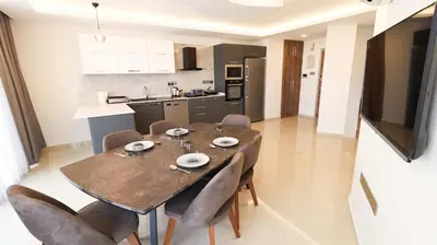 a dining room table with chairs and a kitchen at Girne Merkezde Geniş Teraslı Havuzlu Daire in Alsancak
