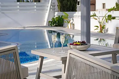 a table with wine glasses and a bowl of fruit next to a swimming pool at Villa Amy - 100m from Nisia Loumbardi Beach in Protaras