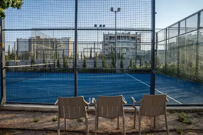 a tennis court seen through a fence with two chairs at Luxe One Residence in Aglantzia
