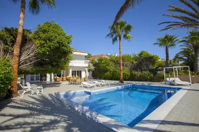 a swimming pool with palm trees and a house at Meneou Beachfront Villa Sunset in Pervolia