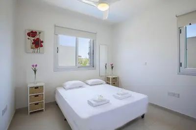 a white bedroom with a bed and two windows at Villa Posidonas 3 in Protaras