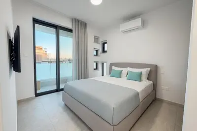 a white bedroom with a bed and a large window at Sunrise Pearl - 2 min walk to Sirena Bay in Paralimni