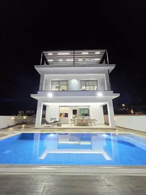 a large white house with a swimming pool at night at Mediterranean Sunrise Villa Protaras in Paralimni