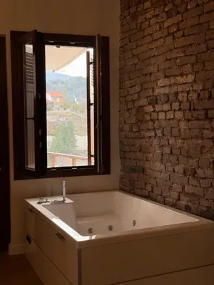 a bath tub in a bathroom with a brick wall at Aprosmeno Jacuzzi House 7 in Agros