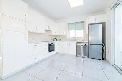 a white kitchen with white cabinets and a refrigerator at Green Bay Villa #12 in Protaras