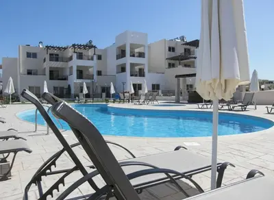 a pool with chairs and umbrellas in front of a building at 2 Bed apartment with huge balcony overlooking pool in Paralimni