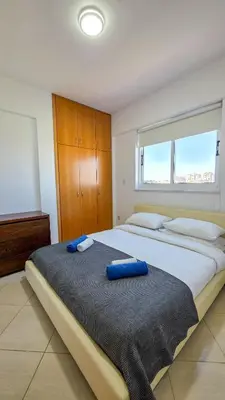 a bedroom with a large bed with blue pillows on it at Sunset Poolside Apartment with Pool facility in Larnaka