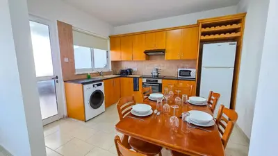 a kitchen with a wooden table with chairs and a dining room at Sunset Poolside Apartment with Pool facility in Larnaka