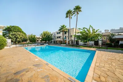 a swimming pool in a courtyard with palm trees and buildings at Trinidad, 1 - A in Paralimni
