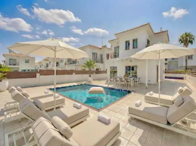 a villa with a swimming pool with chairs and umbrellas at Fig Tree Beach Villa One in Protaras