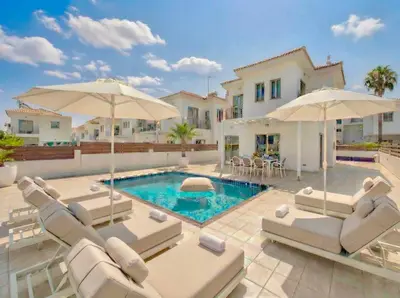 a villa with a swimming pool with chairs and umbrellas at Fig Tree Beach Villa One in Protaras