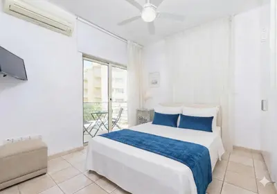 a white bedroom with a bed and a tv at Fig Tree Beach Villa Four in Protaras