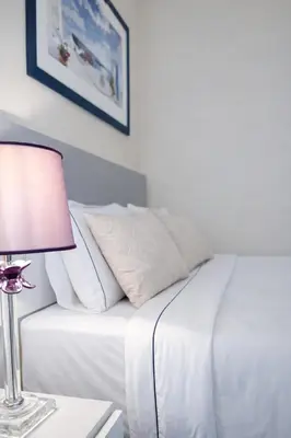 a bed with white sheets and a lamp on a table at Gulf Beach Apartment by TrulyCyprus in Limassol