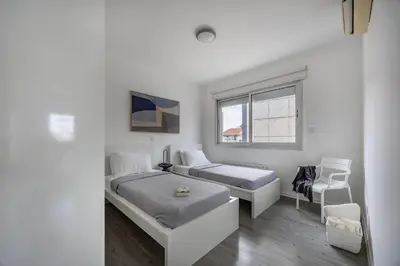 a white bedroom with two beds and a chair at Vasileos Konstantinou Modern 2BR City Apartment with Balcony in Limassol