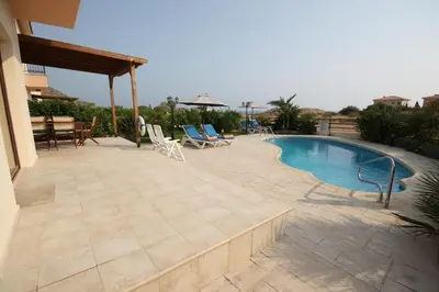 a patio with a pool and chairs and a table at Bay Villas in Pissouri