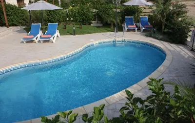a swimming pool with chairs and umbrellas in a yard at Bay Villas in Pissouri