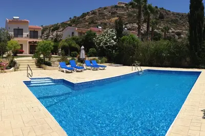 a swimming pool with blue chairs and a house at Bay Villas in Pissouri