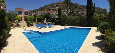a swimming pool with blue chairs and a house at Bay Villas in Pissouri