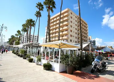 a sidewalk with tables and umbrellas and palm trees at Ithaki Phinikoudes Apartment 307 in Larnaka