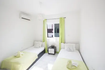 two beds in a room with white walls and yellow curtains at Broadway Villas in Protaras