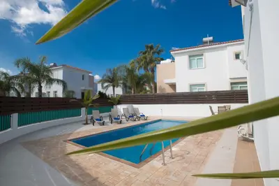 a swimming pool next to a white building at Halle Villa in Protaras