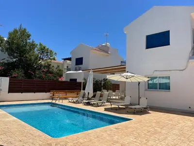 a swimming pool with chairs and an umbrella next to a house at Sol y Mar Malama Villa in Paralimni