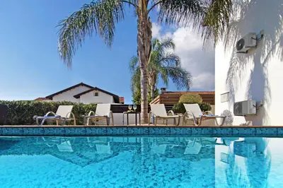 a pool with chairs and palm trees next to a house at Villa Regina in Ayia Napa