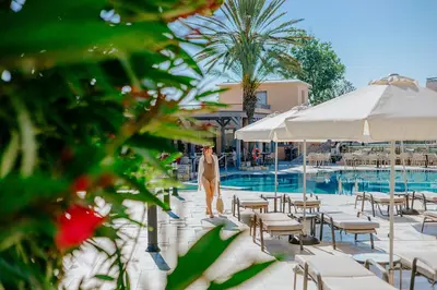 a woman walking by a pool with chairs and umbrellas at Louis St. Elias Resort & Waterpark in Protaras