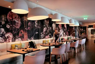 a woman standing in a restaurant with tables and chairs at Royal Apollonia by Louis Hotels in Limassol