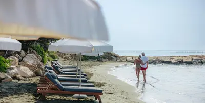 a group of lounge chairs and umbrellas on a beach at Royal Apollonia by Louis Hotels in Limassol
