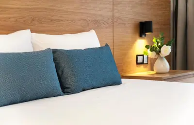 a bed with two blue pillows and a vase with flowers at Ajax Hotel in Limassol