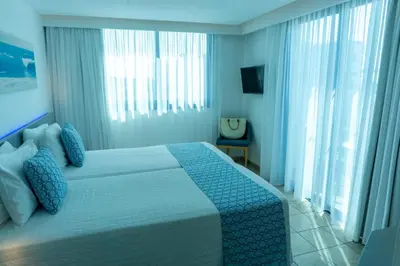 a bedroom with a bed with blue sheets and windows at Anonymous Beach Hotel (Adults 16+) in Ayia Napa