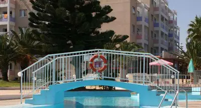 a blue bridge over a swimming pool in front of a building at Astreas Beach Hotel Apartments in Protaras