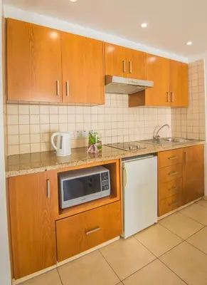 a kitchen with wooden cabinets and a microwave at Alva Hotel Apartments in Protaras