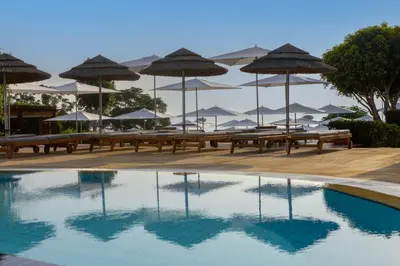 a pool with benches and umbrellas on a beach at Capo Bay Hotel in Protaras