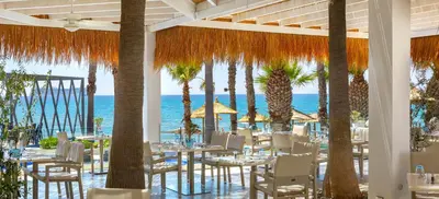 a restaurant with tables and chairs and palm trees at The GrandResort - Leonardo Limited Edition in Limassol