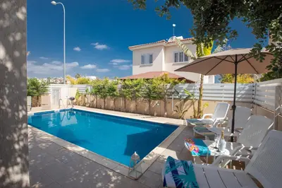 a swimming pool with chairs and an umbrella next to a house at George's Lux Villa in Protaras