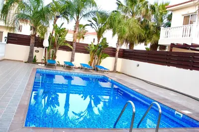 a swimming pool with blue chairs and palm trees at Villa Agnes in Ayia Napa