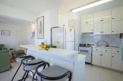 a kitchen with white cabinets and a counter with a glass of wine at Protaras Holiday Suite Annie in Protaras