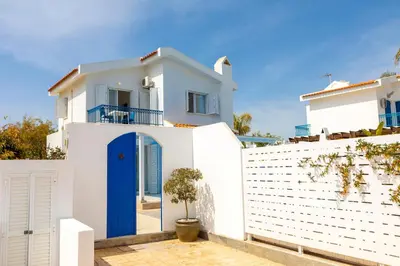 a white house with a blue door and a fence at Fig Tree Bay Villa 3 in Protaras