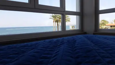 a bedroom with windows and a blue bed with a view of the ocean at Periyiali Beach Sunset Suite A7 in Pervolia