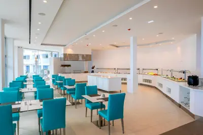 a cafeteria with blue chairs and tables and a kitchen at Limanaki Beach Hotel & Suites in Ayia Napa