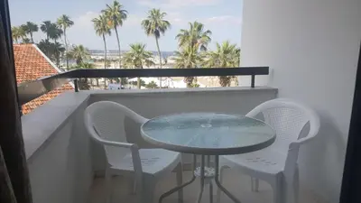 a table and chairs on a balcony with palm trees at Alex Beach Apartment 203 in Larnaka