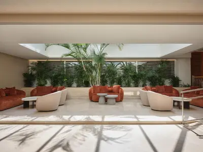 a lobby with orange chairs and tables and plants at Atlantica Oasis Hotel in Limassol