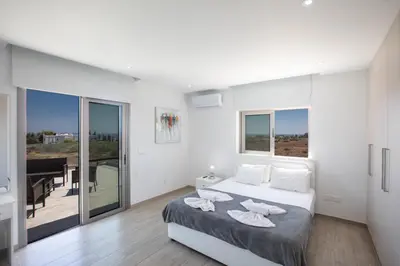 a white bedroom with a bed and a balcony at Villa Marylou in Protaras
