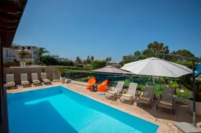 a swimming pool with chairs and an umbrella at Villa Ricky in Protaras