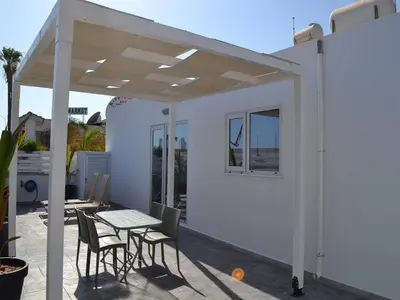 a white pergola on a patio with a table and chairs at Makronissos Beach Studio in Ayia Napa