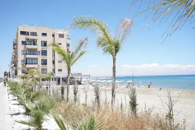 a beach with palm trees and a building at Lazuli Sea View-Beachfront Ap 405 in Larnaka